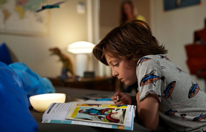Kid reading in room with lamp on.