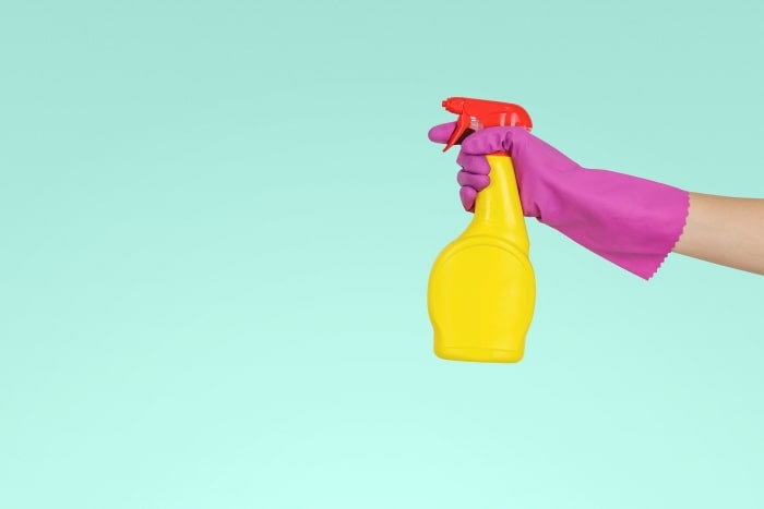 Hand with rubber glove holding household cleaner.
