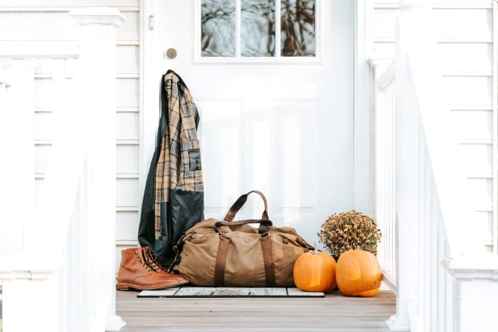Brown duffel bag, boots and jacket on fall porch.