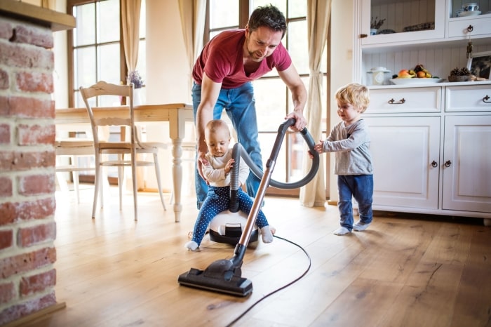 Dad vacuums kitchen with two toddlers.