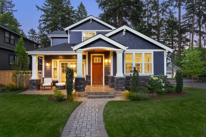 Blue Craftsman style home with exterior lights on.