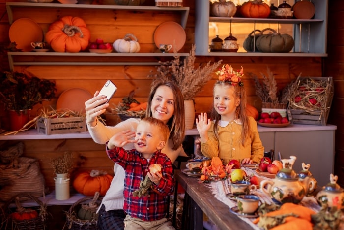 Mom with two children holding up phone to FaceTime family at Thanksgiving table.