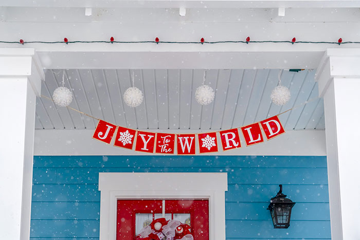 Blue house decorated for Christmas with red front door and red Joy to the World holiday banner.