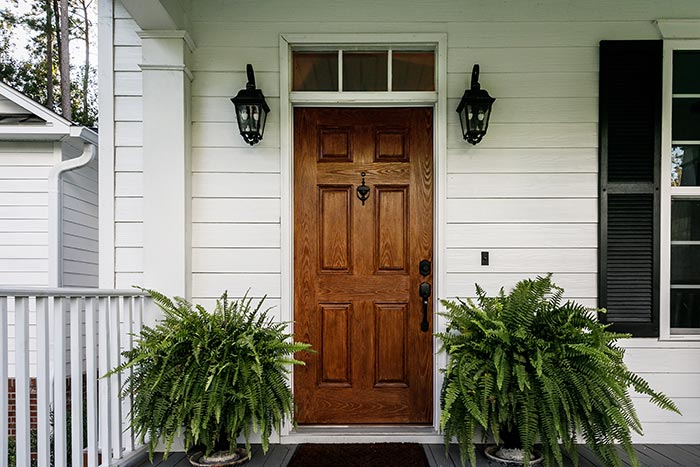 Front porch of white home with wood front door and potted ferns.