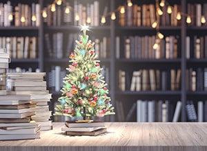 Library of books with small Christmas tree on table.