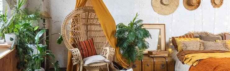 Bohemian bedroom with wicker chair, plants and hats on wall.