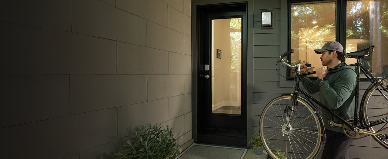 Man carrying a bike walks up to a door with the Schlage Sense Pro UWB smart lock for hands-free unlocking
