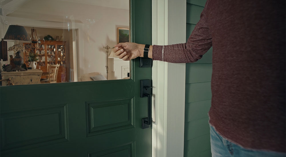 Green front entry way with man unlocking his Schlage deadbolt with a smart watch