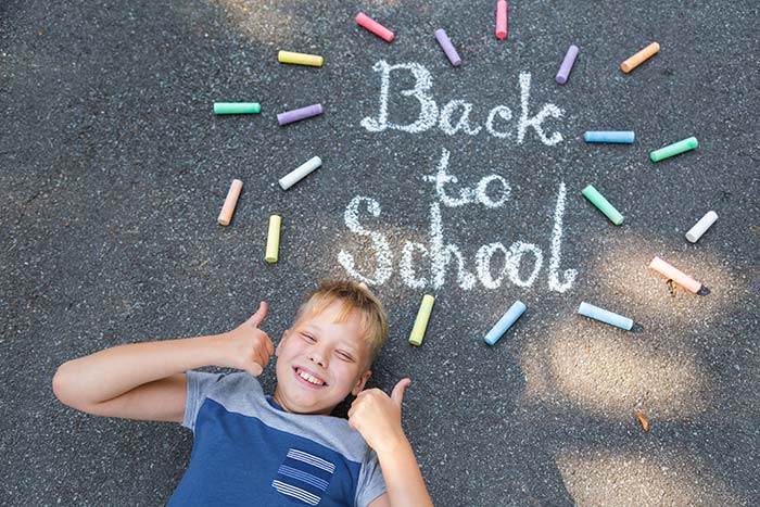 Boy laying on driveway smiling for camera next to Back to School written in sidewalk chalk.