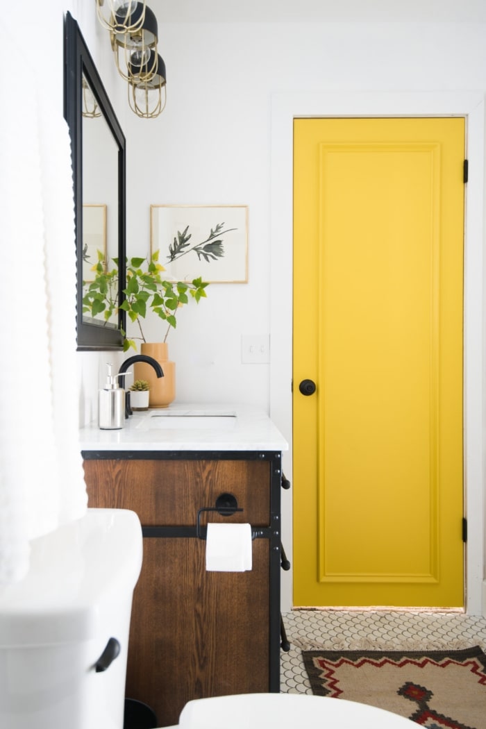 Yellow bathroom door with faux paneling and black lock.