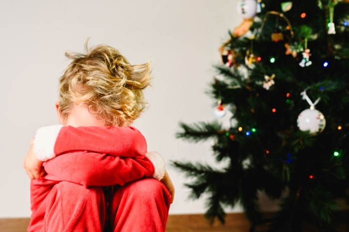 Kid pouting next to Christmas tree.