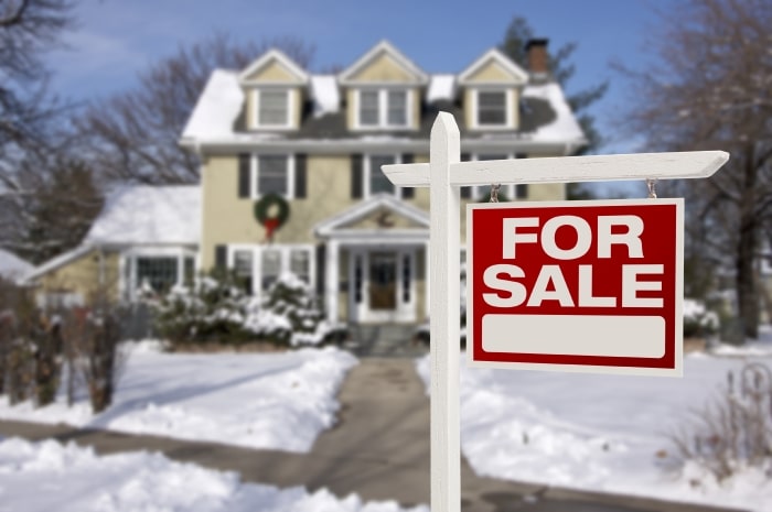 For sale sign in front of house covered in snow.