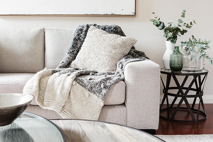 Cozy light grey living room couch with blanket and end table with vases and floral decor.