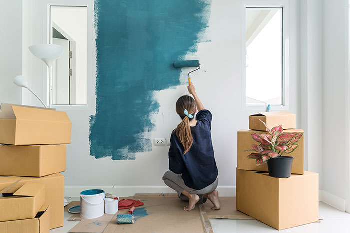 Woman next to moving boxes painting walls teal.