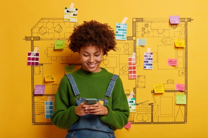 Woman looking at smartphone next to home design plans.