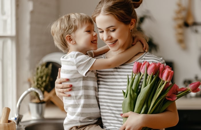 Mother hugging son while holding bouquet of tulips.