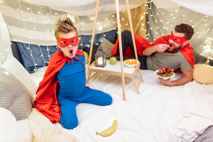 Father and son playing and eating inside blanket fort.