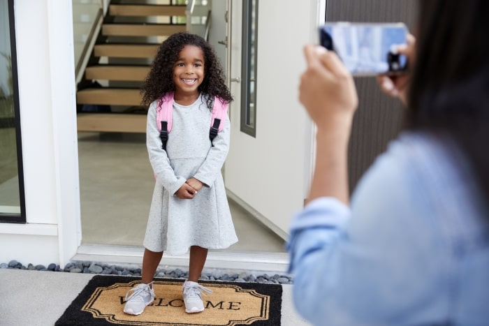 Little girl smiling at front door on first day of school.