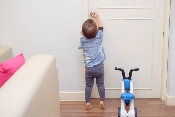 Toddler reaching up to touch door lock.