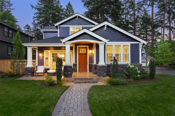 Blue Craftsman style home with exterior lights on.