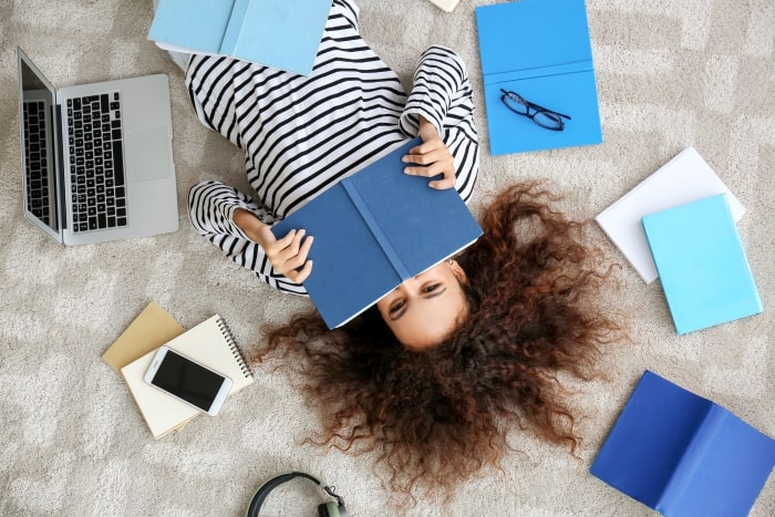 College student laying on bed with notebooks and computer.