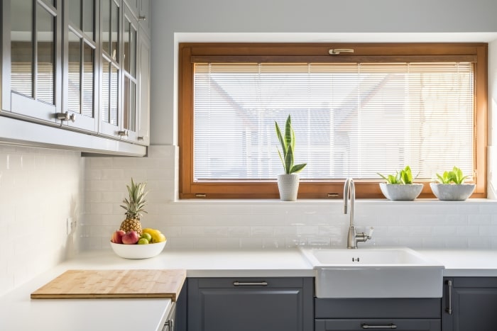 Clean, minimalist kitchen with grey cabinets and large window above farmhouse sink.