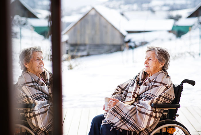 Woman sitting on deck outside in wheelchair while wrapped in blanket during winter.