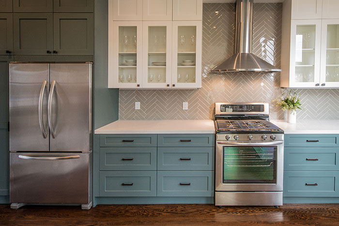 Modern kitchen with two toned cabinets, stainless steel appliances and herringbone backsplash.