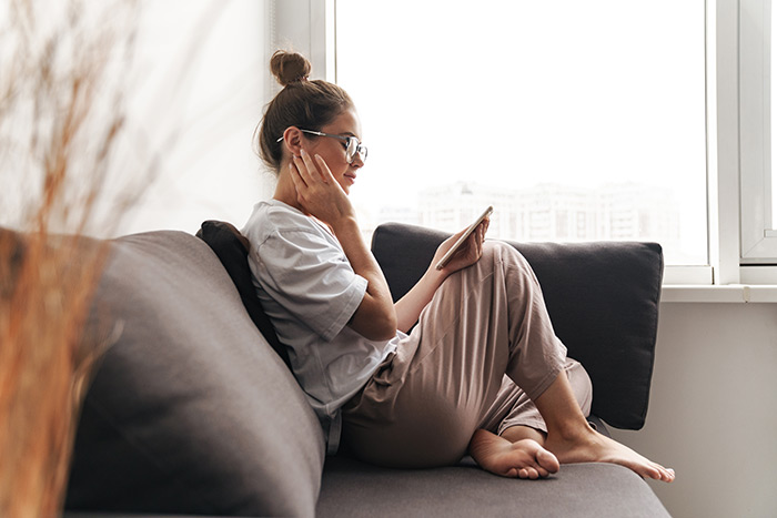 Woman in loungewear sitting on couch looking at phone.