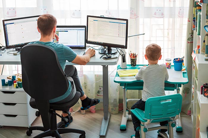Father working from home next to son at kids desk.