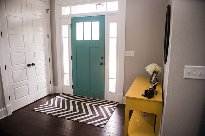 Entryway with chevron rug, yellow table and teal front door.