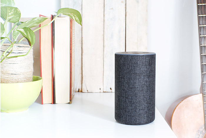 Amazon Echo speaker with Alexa on dresser next to books.