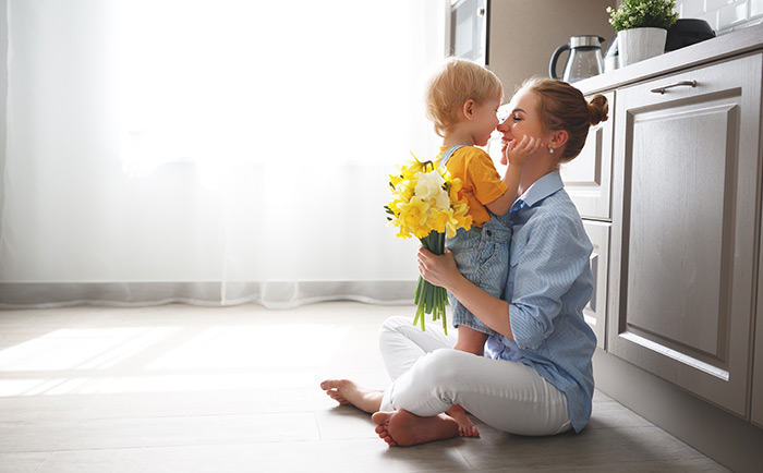 Mother holding bouquet of daffodils while hugging toddler son.