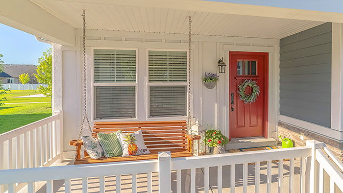 Suburban front porch with porch swing and red orange front door decorated for summer.
