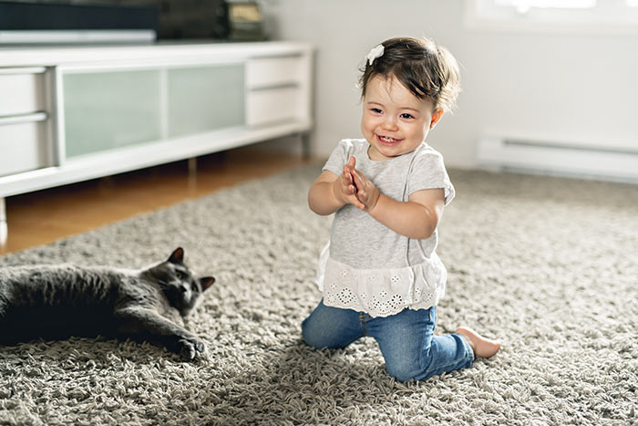 Toddler girl playing with cat on floor.
