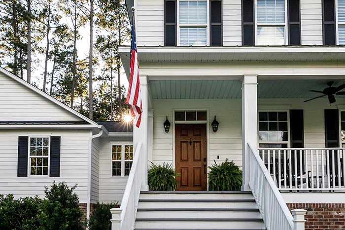 White farmhouse with black shutters and front porch with wood doors.