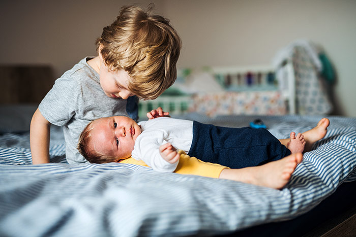 Toddler and baby brother on bed