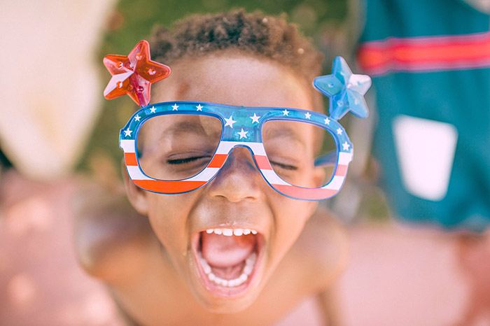 Young boy playing in water outside while wearing patriotic glasses.