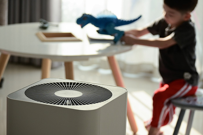 Air purifier to reduce home allergies and little boy playing with dinosaurs.