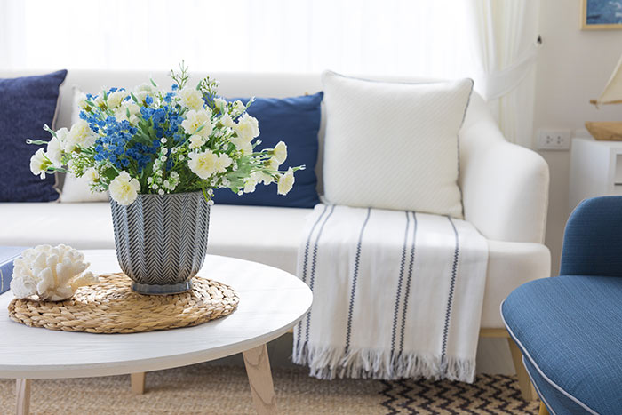 Flowers in a pot and decoration on a table with blue pillows on fabric sofa in living room.