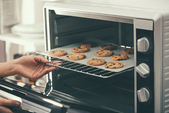 Woman taking out baking tray with cookies from oven.