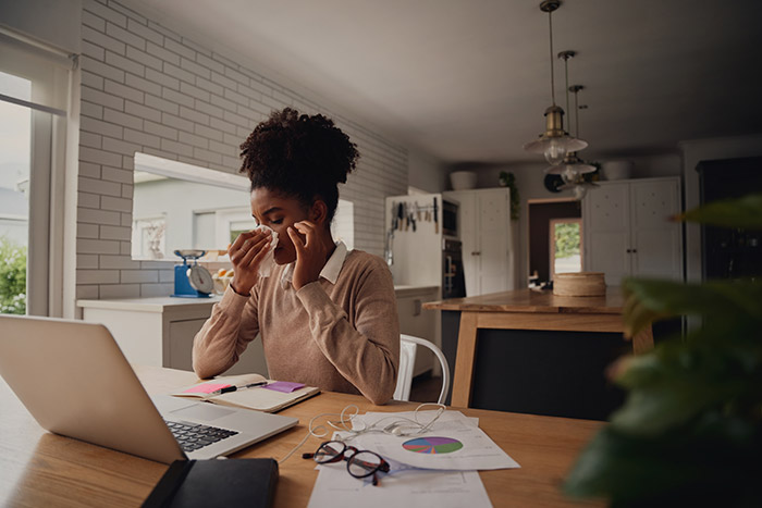 Woman blowing nose at kitchen table while working from home.