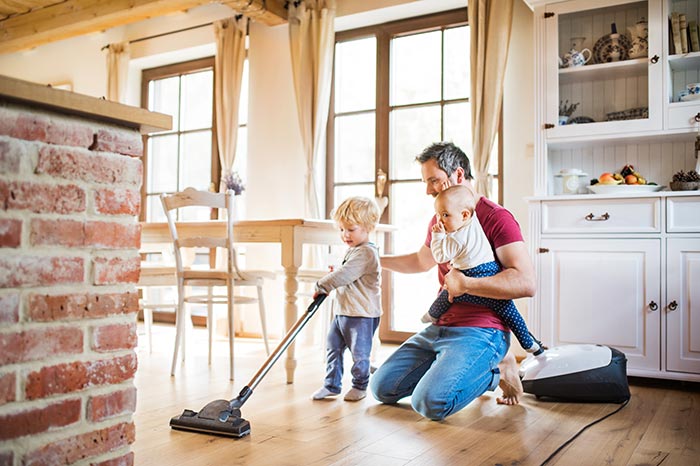Father vacuuming floor with two young children.