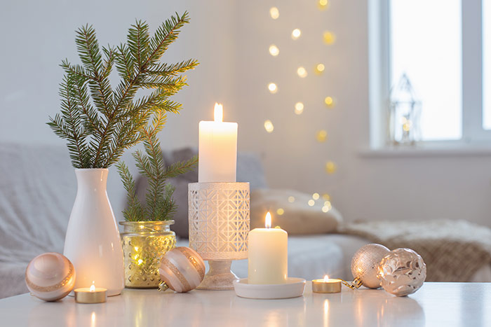 Lit candles next to vase of Christmas greenery and holiday ornaments.