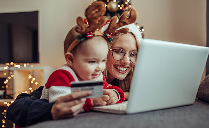Mom and baby looking at laptop while holding credit card and wearing Christmas clothing.