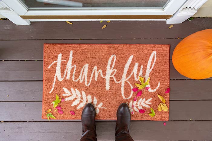 Thanksgiving front door mat that says Thankful next to pumpkin.