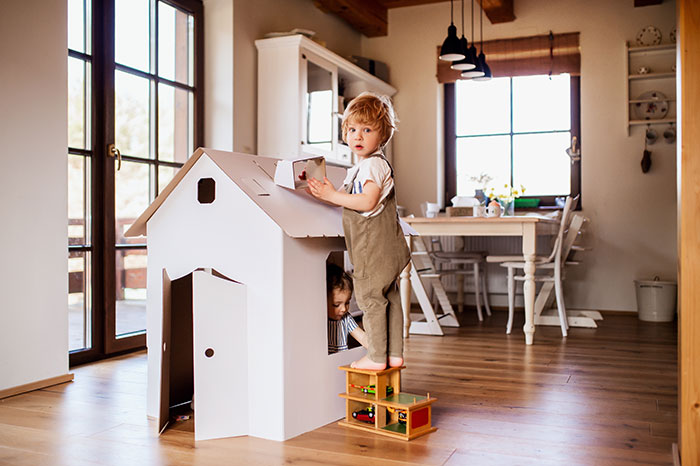 Toddlers reusing cardboard box for DIY playhouse.