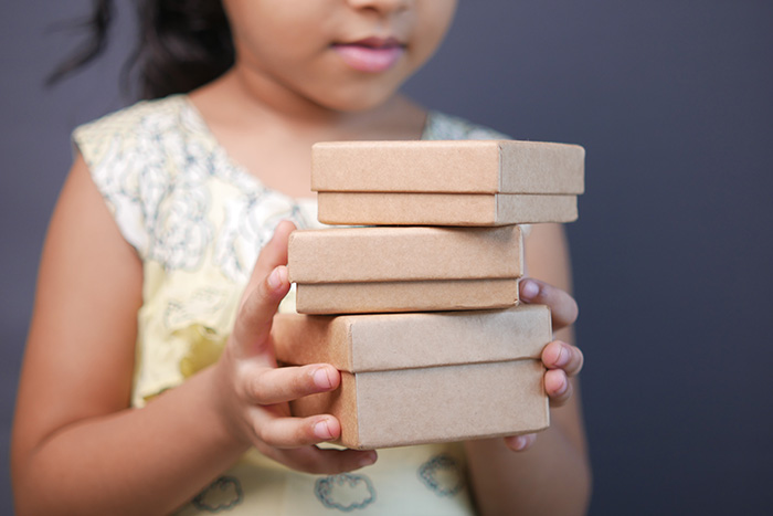 young girl holding stack of cardboard gift boxes.
