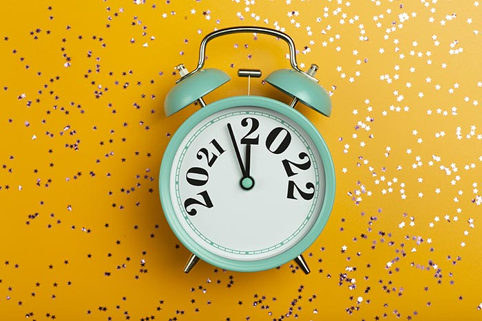 2021 changes to 2022 on an alarm clock on a yellow background with festive glitter on New Year's Eve and Christmas.