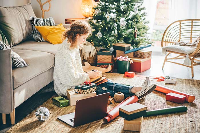 Woman writing in notebook while sitting on floor surrounded by holiday gift wrap.